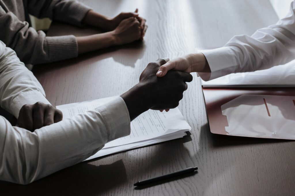 Business agreement with a handshake over contract documents at a meeting table.